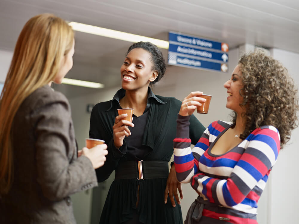 three female office employees chatting while drinking coffee